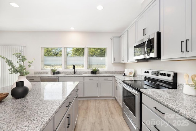 kitchen with stainless steel appliances, light stone countertops, sink, and white cabinets