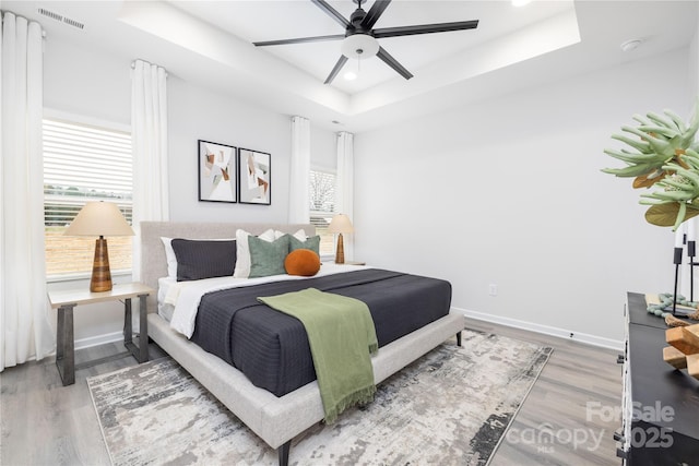 bedroom with a ceiling fan, wood finished floors, visible vents, baseboards, and a raised ceiling