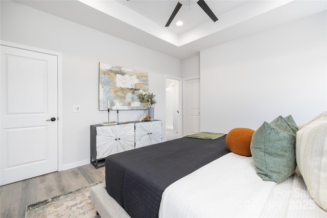 bedroom featuring a raised ceiling, a ceiling fan, wood finished floors, recessed lighting, and baseboards