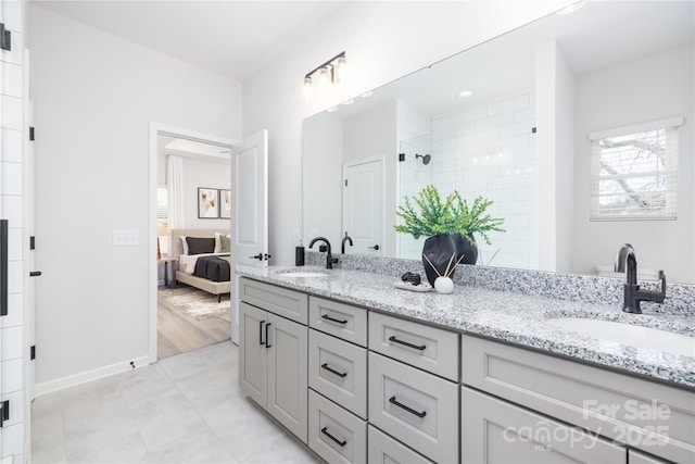 bathroom with double vanity, tiled shower, ensuite bathroom, and a sink