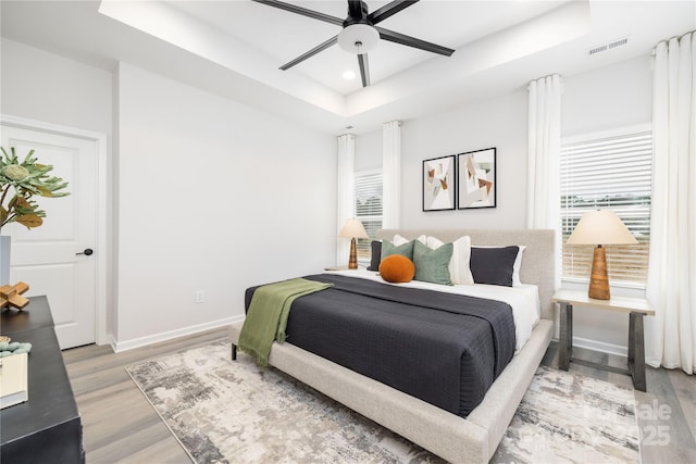 bedroom with visible vents, multiple windows, light wood-style flooring, and a tray ceiling