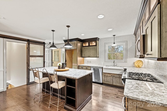 kitchen featuring pendant lighting, appliances with stainless steel finishes, light stone counters, and a kitchen island