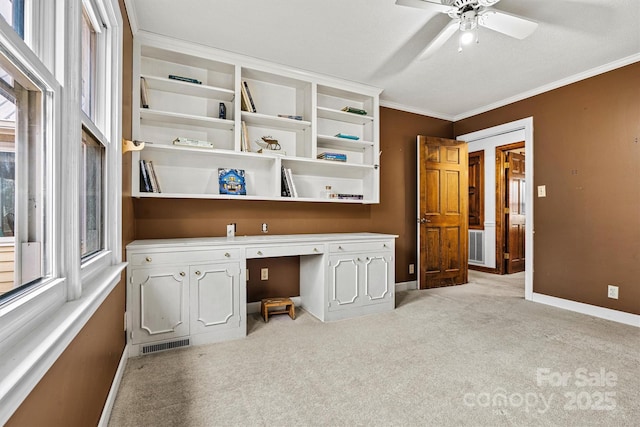 unfurnished office featuring crown molding, a healthy amount of sunlight, built in desk, and light carpet