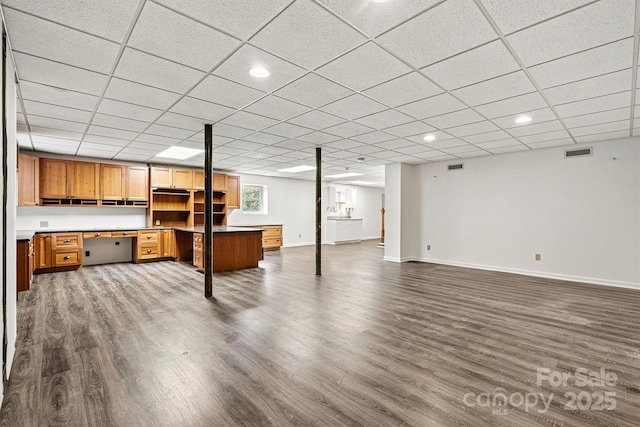 basement with dark wood-type flooring, a paneled ceiling, and built in desk