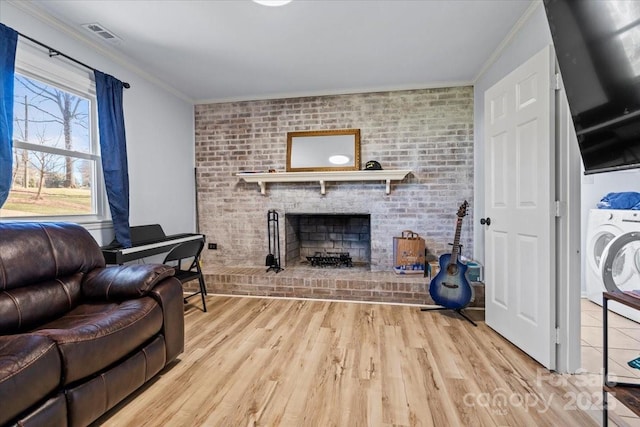 living room featuring brick wall, a fireplace, washer / dryer, crown molding, and light wood-type flooring