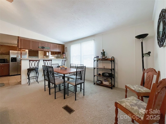 dining space featuring lofted ceiling, light colored carpet, and a textured ceiling