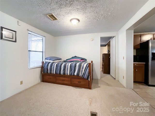 bedroom featuring light carpet, a textured ceiling, and stainless steel refrigerator with ice dispenser