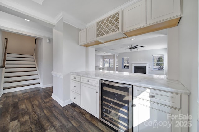 bar featuring dark wood-type flooring, ceiling fan, white cabinetry, ornamental molding, and beverage cooler