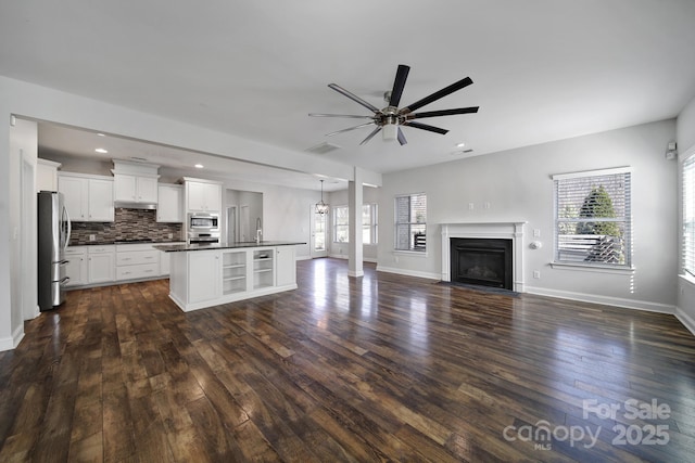 kitchen with appliances with stainless steel finishes, dark hardwood / wood-style floors, white cabinetry, an island with sink, and backsplash