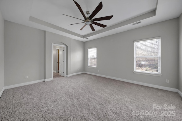 carpeted spare room with a raised ceiling and ceiling fan