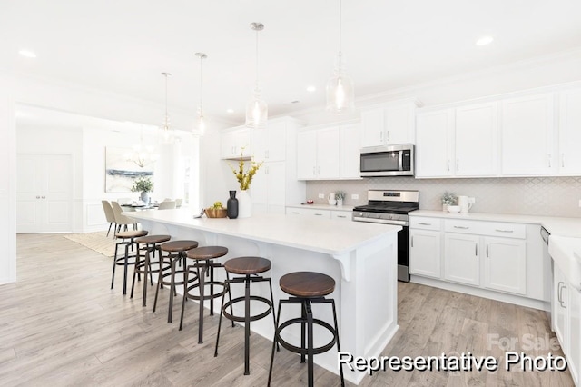 kitchen with decorative light fixtures, a center island, white cabinets, and appliances with stainless steel finishes