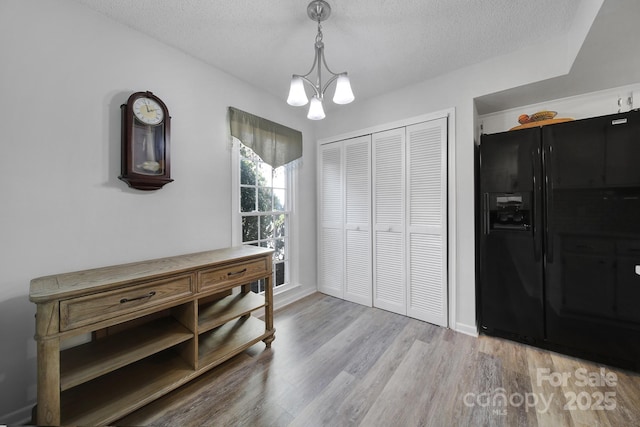 bedroom with a closet, wood-type flooring, black fridge with ice dispenser, and a textured ceiling