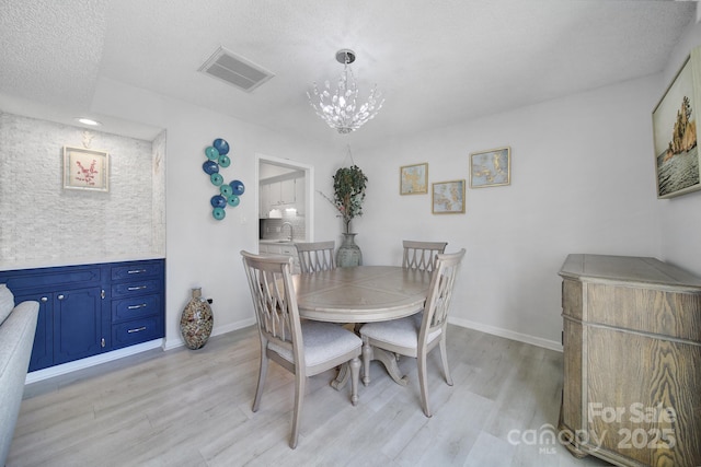 dining space with a notable chandelier, light hardwood / wood-style flooring, sink, and a textured ceiling