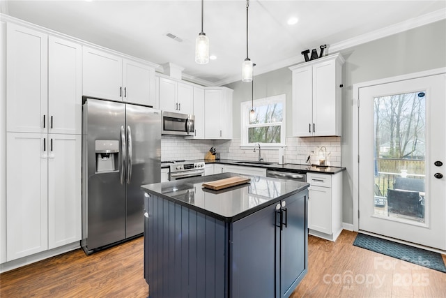 kitchen featuring sink, appliances with stainless steel finishes, hanging light fixtures, ornamental molding, and white cabinets