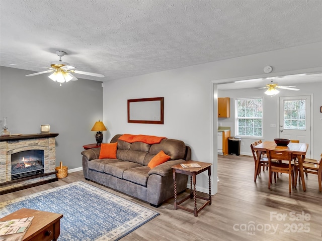 living room with a fireplace, ceiling fan, and light wood-type flooring