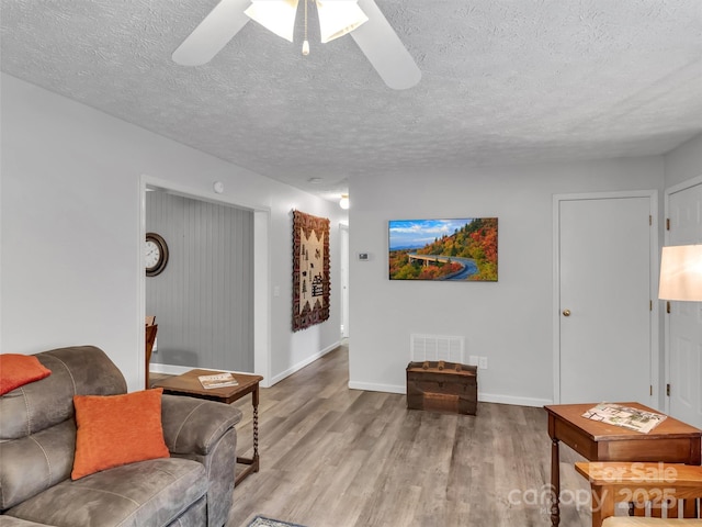 living room featuring ceiling fan, a textured ceiling, and light hardwood / wood-style floors