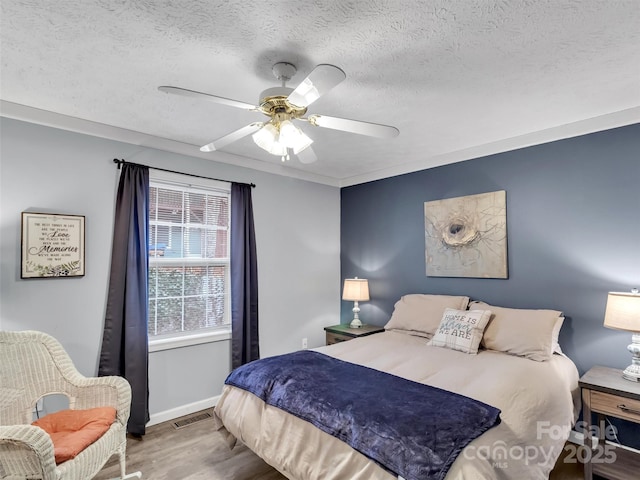 bedroom with ceiling fan, wood-type flooring, and a textured ceiling