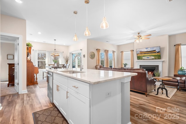 kitchen with stainless steel dishwasher, light wood-style floors, white cabinetry, a sink, and a warm lit fireplace