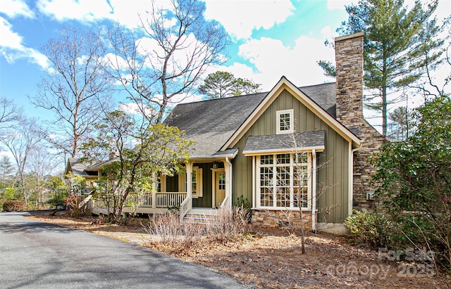 view of front of property featuring a porch, a chimney, a shingled roof, and board and batten siding