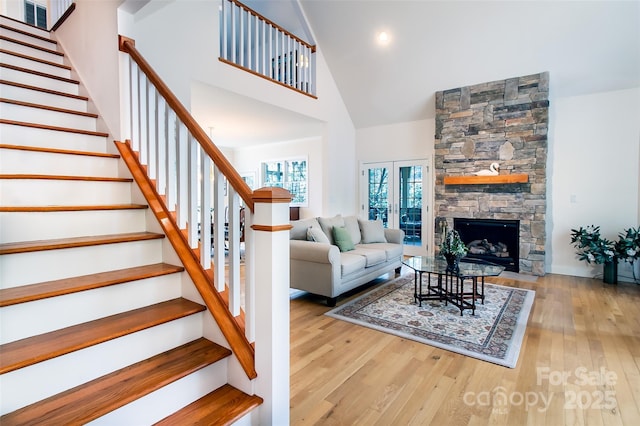 living area with a fireplace, high vaulted ceiling, stairway, and light wood-style flooring