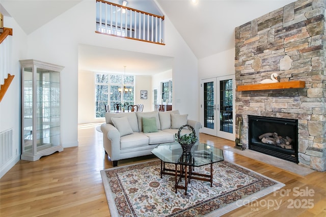 living room with light wood-style flooring, an inviting chandelier, french doors, and a stone fireplace