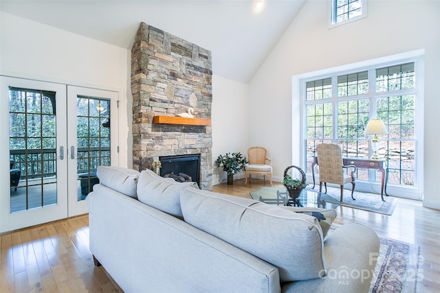 living area featuring a wealth of natural light, high vaulted ceiling, french doors, and a stone fireplace