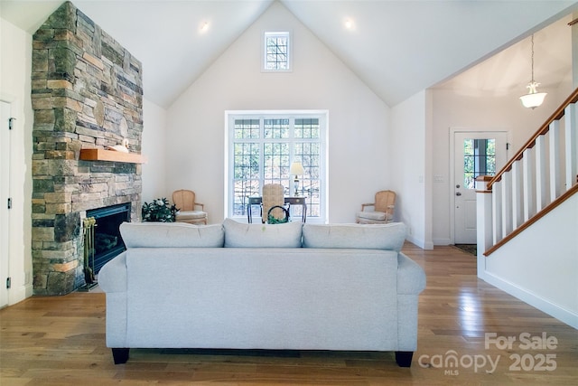 living area with stairs, wood finished floors, baseboards, a fireplace, and high vaulted ceiling