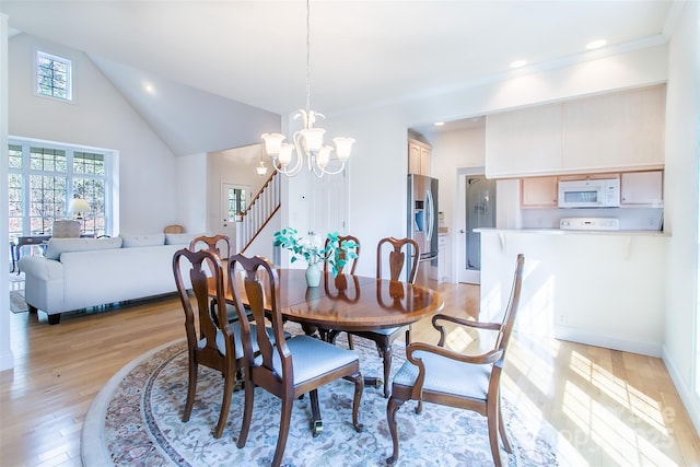 dining space featuring recessed lighting, light wood-style flooring, an inviting chandelier, high vaulted ceiling, and stairs