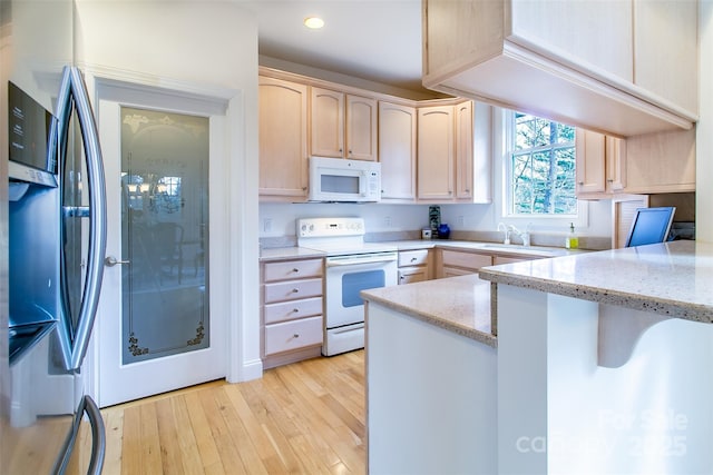 kitchen featuring light brown cabinets, a peninsula, white appliances, light wood-type flooring, and light stone counters