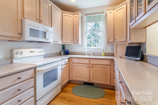 kitchen with light stone countertops, white appliances, light brown cabinets, and a sink