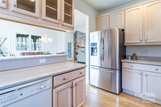 kitchen featuring white dishwasher, stainless steel fridge with ice dispenser, light brown cabinetry, and glass insert cabinets