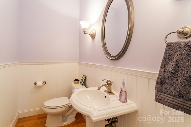 bathroom featuring toilet, wainscoting, wood finished floors, and a sink