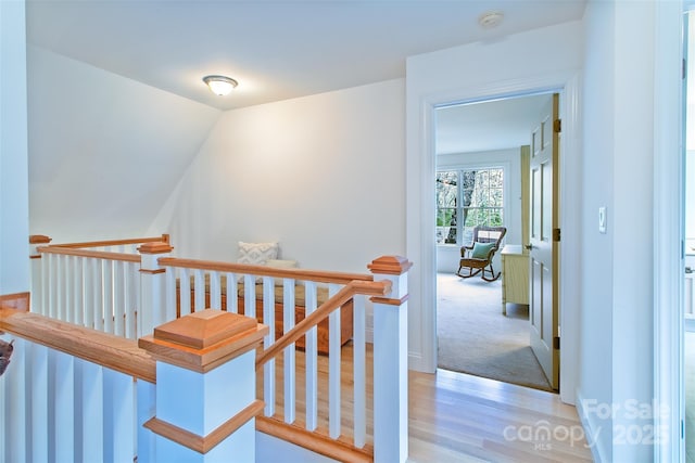 hall with an upstairs landing, lofted ceiling, and light wood-style floors