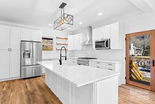 kitchen with wall chimney range hood, sink, appliances with stainless steel finishes, hanging light fixtures, and white cabinets