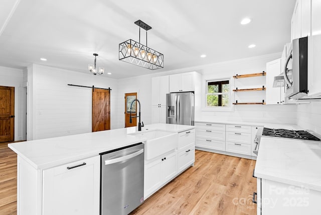 kitchen with stainless steel appliances, an island with sink, white cabinets, and a barn door