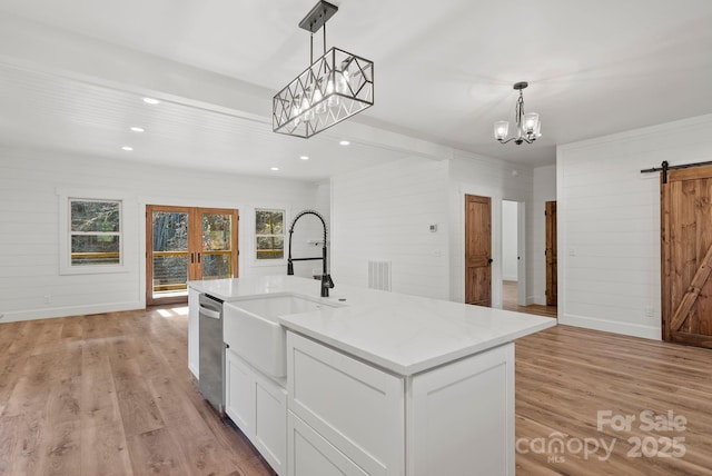 kitchen featuring white cabinetry, hanging light fixtures, a barn door, and a center island with sink