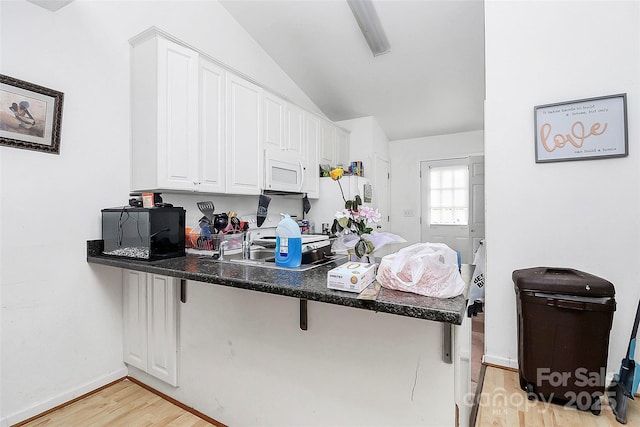 kitchen with white cabinetry, lofted ceiling, a breakfast bar area, light hardwood / wood-style floors, and kitchen peninsula