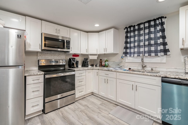 kitchen featuring white cabinets, light stone counters, appliances with stainless steel finishes, light wood-style floors, and a sink