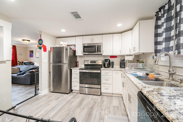 kitchen featuring stainless steel appliances, visible vents, white cabinetry, a sink, and light wood-type flooring