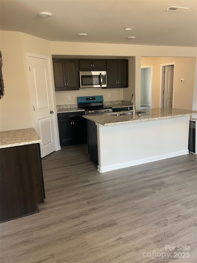 kitchen with light stone counters, appliances with stainless steel finishes, sink, and a center island with sink