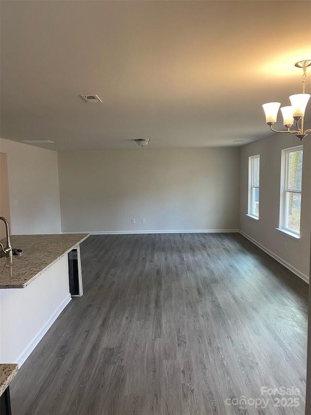 unfurnished living room featuring an inviting chandelier, sink, and dark hardwood / wood-style floors