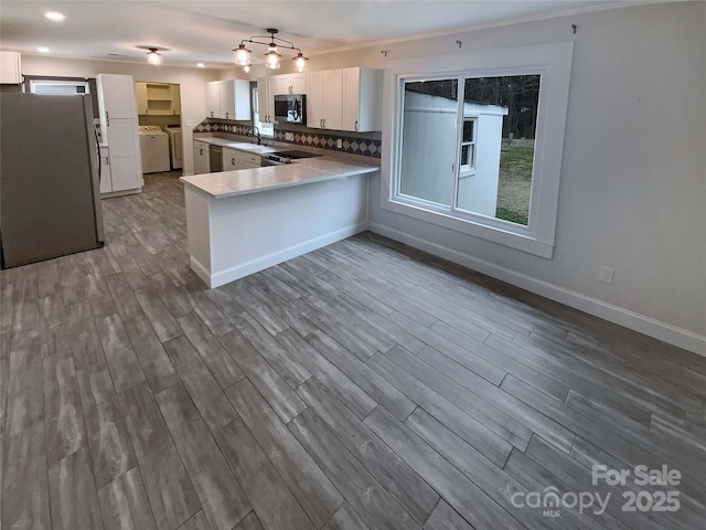 kitchen featuring separate washer and dryer, kitchen peninsula, stainless steel appliances, hardwood / wood-style floors, and white cabinets