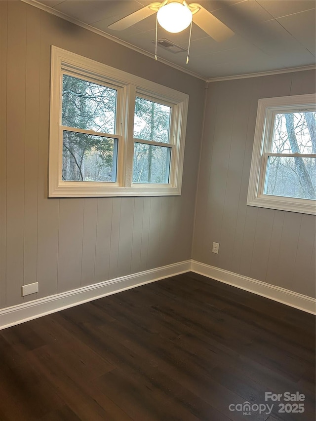 spare room featuring dark wood-style flooring, crown molding, visible vents, a ceiling fan, and baseboards