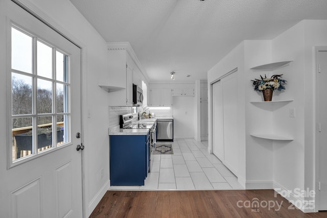 kitchen featuring blue cabinets, white cabinetry, light hardwood / wood-style floors, stainless steel appliances, and a textured ceiling