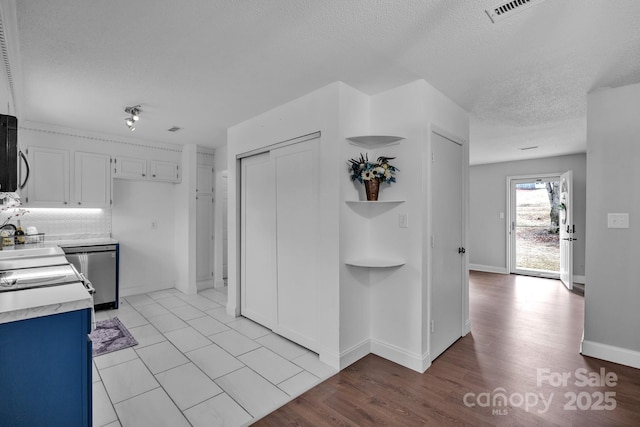 kitchen featuring dishwasher, backsplash, white cabinets, a textured ceiling, and light hardwood / wood-style flooring