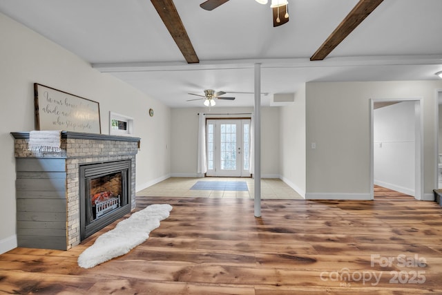 living room featuring beamed ceiling, ceiling fan, wood-type flooring, and a brick fireplace