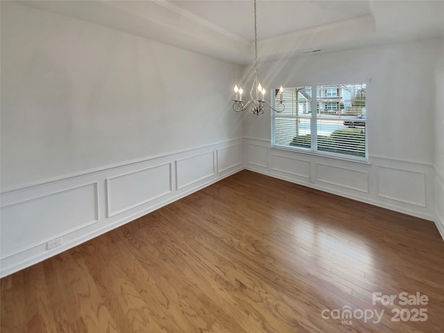 unfurnished dining area with a raised ceiling, wood-type flooring, and a chandelier