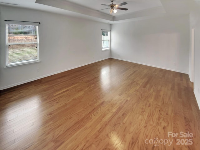 empty room featuring a raised ceiling, wood-type flooring, and ceiling fan