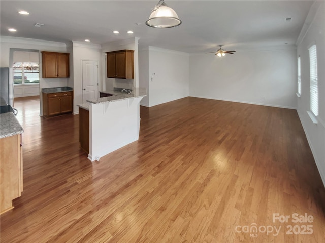 kitchen with a breakfast bar, hardwood / wood-style flooring, ornamental molding, pendant lighting, and light stone countertops