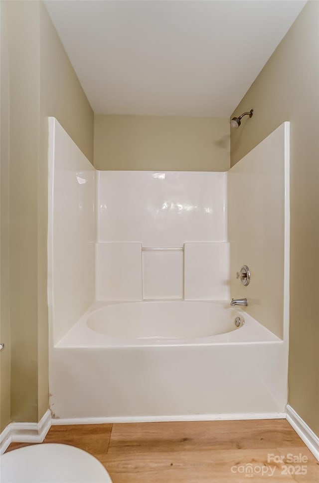 bathroom with hardwood / wood-style flooring,  shower combination, and toilet